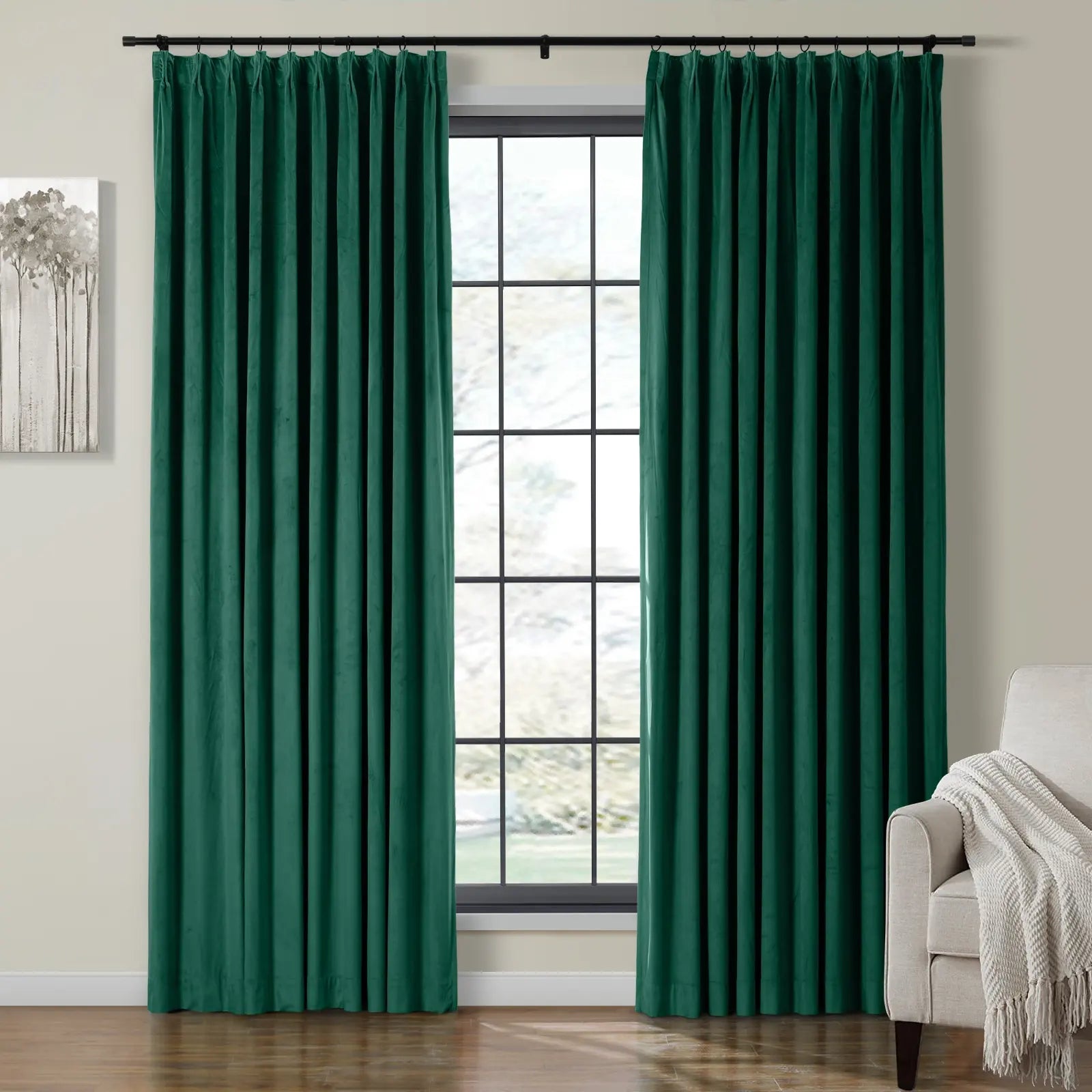 Two luxurious dark emerald green velvet curtains on a black rod frame a grid-pane window with a subtle outdoor blur, complemented by an abstract grey tree painting and a beige armchair with a cream fringed throw