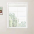 Photograph of a white window with a light grey roller blind revealing a blurred outdoor scene of green trees and light sky, alongside a framed Van Gogh art print on a light beige wall