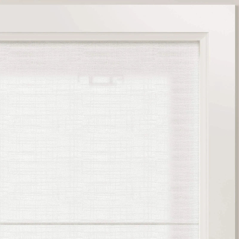 Photograph of a white textured window blind inside a clean white frame showing subtle light filtering