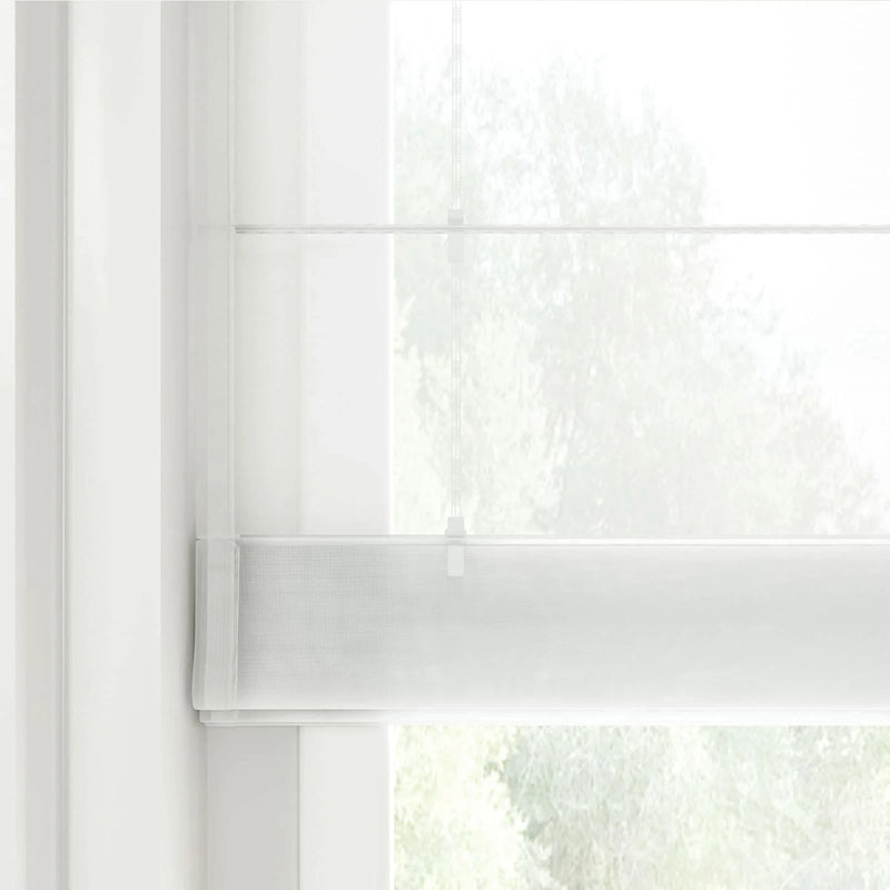 Photograph of a sheer white layered window blind featuring a subtle horizontal weave and thin control cords allowing diffuse light from the blurred green foliage outside
