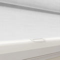 A modern white textured fabric roller blind on a window, featuring a sleek white bottom rail and a clear plastic pull tab