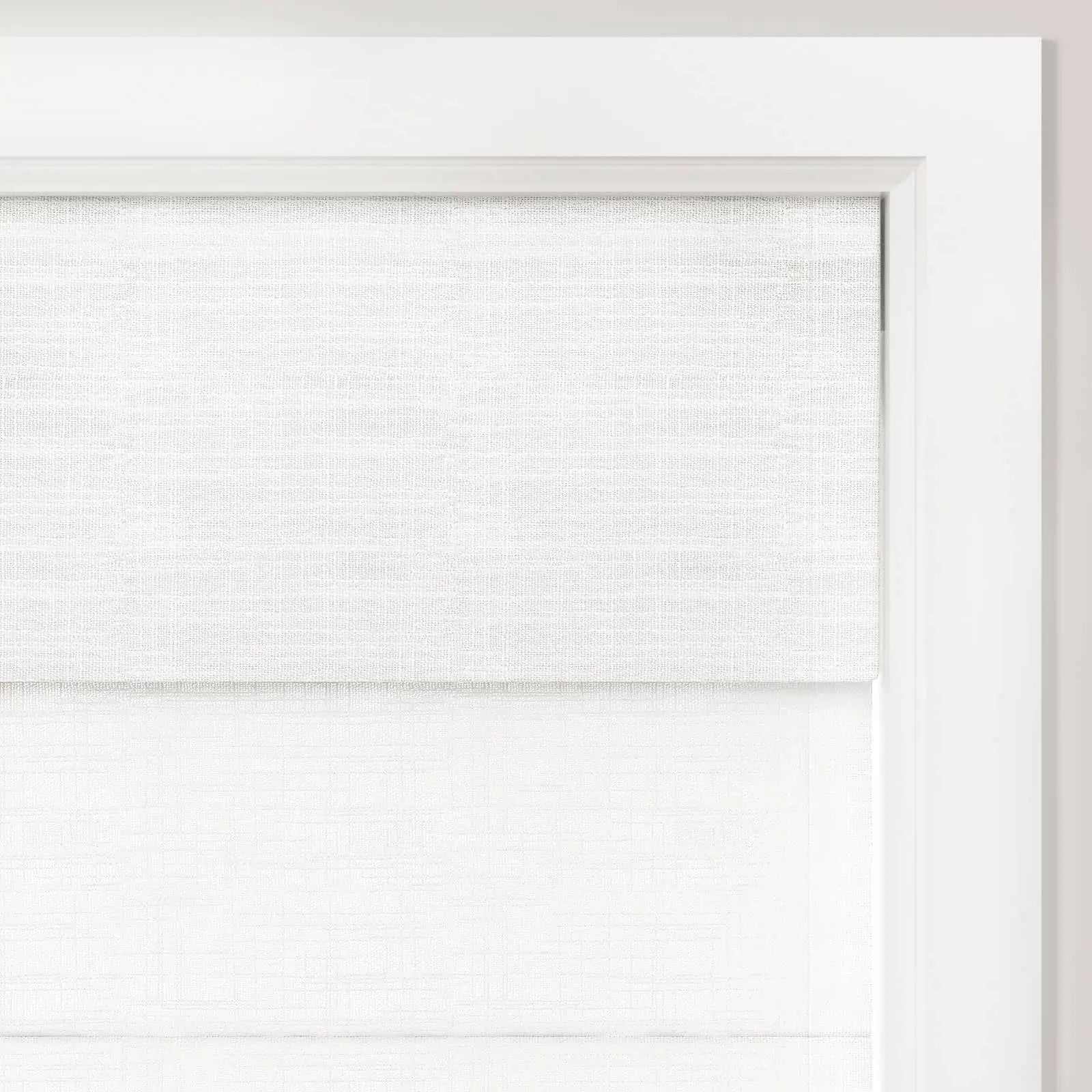 A close-up of a double-layered white textured fabric window shade installed within a bright white wooden window frame providing a minimalist aesthetic