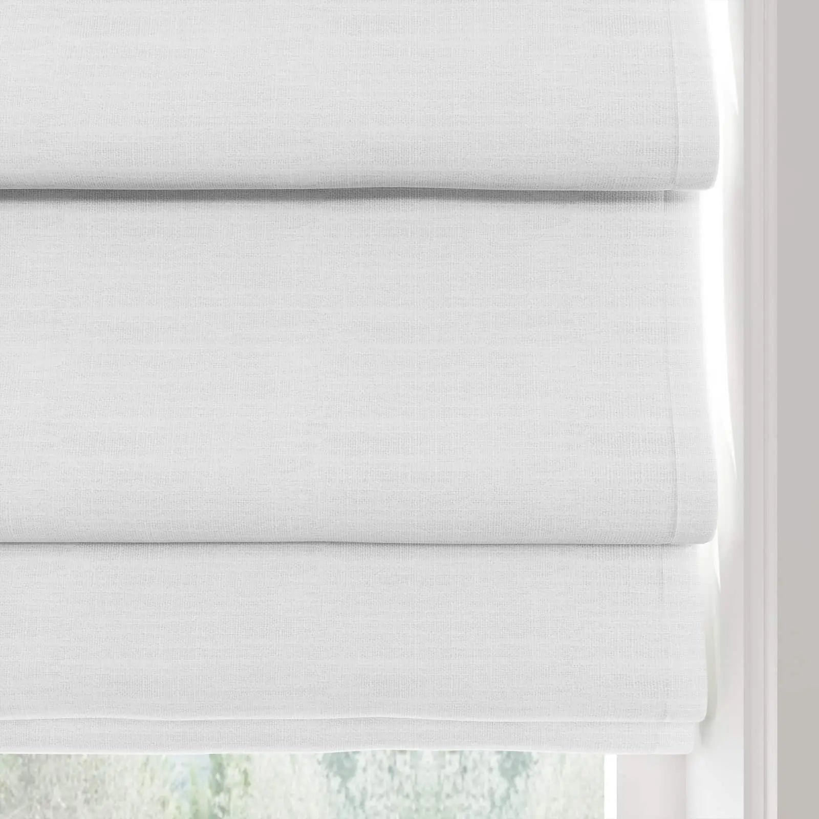 Product image of white textured linen Roman window shades elegantly folded at a bright window with blurred green foliage visible outside