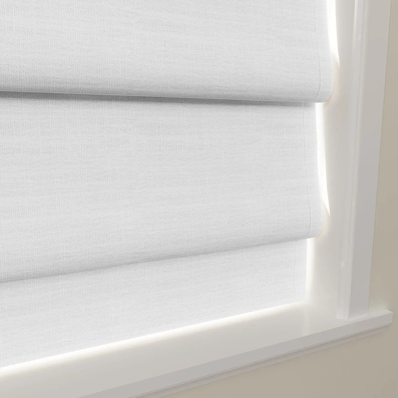 White linen Roman blinds are shown with soft horizontal folds, bathed in bright natural light against a clean white window frame