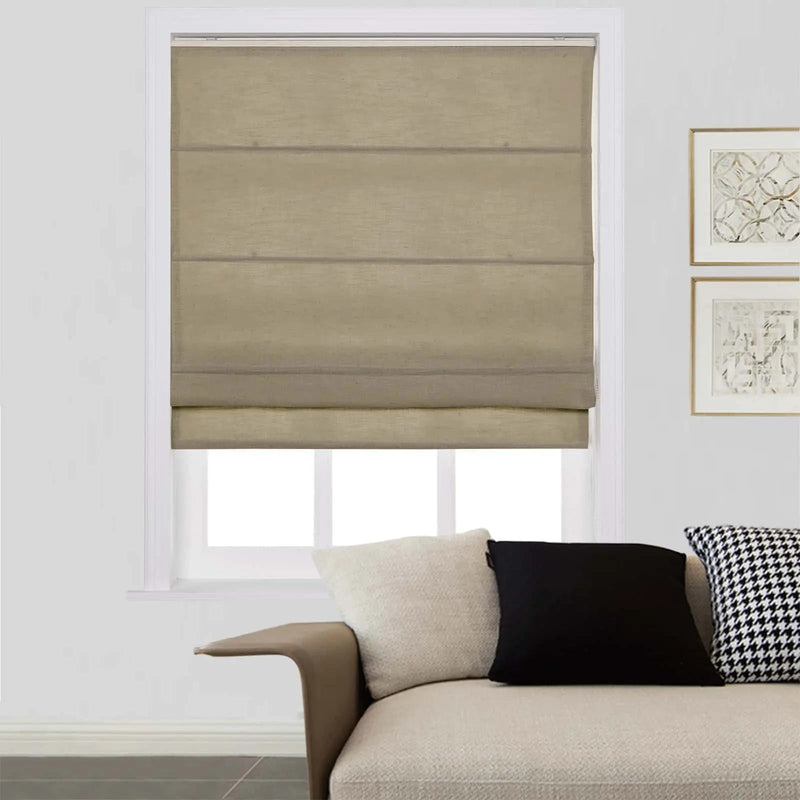 Beige faux linen Roman shade partially covering a window in a modern living room featuring a light-colored sofa with a unique curved armrest, an off-white textured pillow, a solid black pillow, a black and white houndstooth pillow, and two gold-framed abstract artworks on the adjacent wall