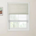 A framed print of a colorful Van Gogh landscape painting on the wall beside a window dressed with a light gray textured Roman blind, a sheer white privacy blind, and a soft green natural view