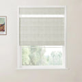 Photograph of a room interior featuring a white-framed window with a light grey textured Roman blind partially lowered over a view of blurred green trees, alongside a framed print of a colorful Van Gogh painting on the adjacent wall