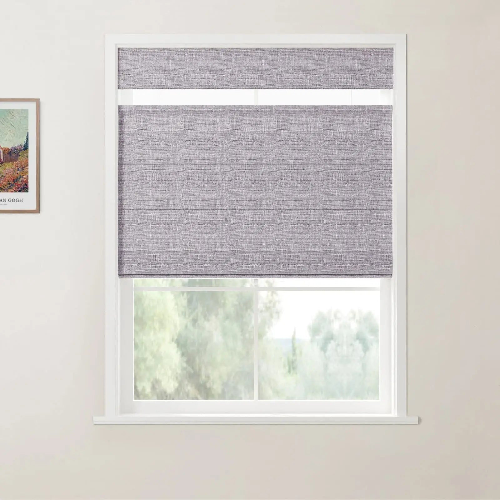 A contemporary interior showcases a window featuring a textured grey pleated roman blind with a top-down, bottom-up functionality, revealing blurred green trees beyond a white frame, adjacent to a light wall displaying a framed Van Gogh print