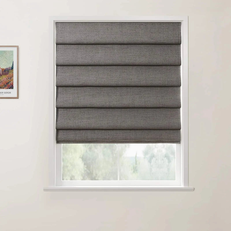 Textile dark gray textured Roman blind covering a window in a light-colored room, partially open to reveal a soft green outdoor landscape, with a framed print of Vincent van Gogh's Wheat Field with Cypresses visible on the adjacent white wall