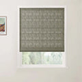 Photograph of a window in an interior room featuring a textured dark gray Roman blind with horizontal folds, set in a white frame, with a partial Van Gogh print on the adjacent wall and blurry green foliage outside