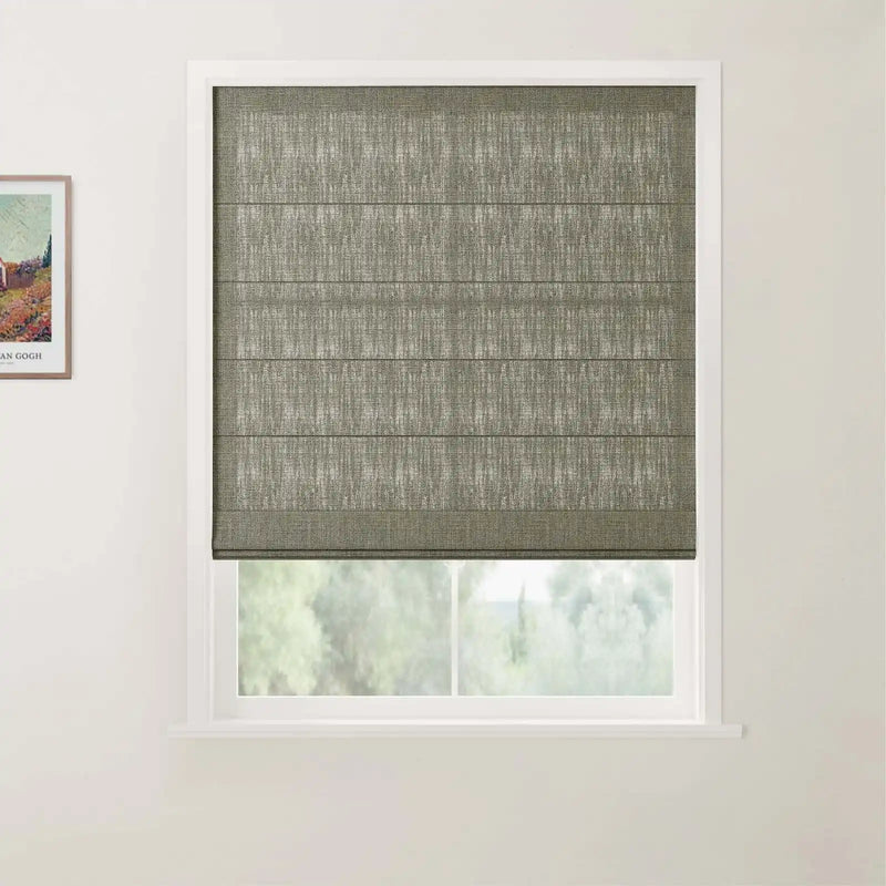 Photograph of a window in an interior room featuring a textured dark gray Roman blind with horizontal folds, set in a white frame, with a partial Van Gogh print on the adjacent wall and blurry green foliage outside