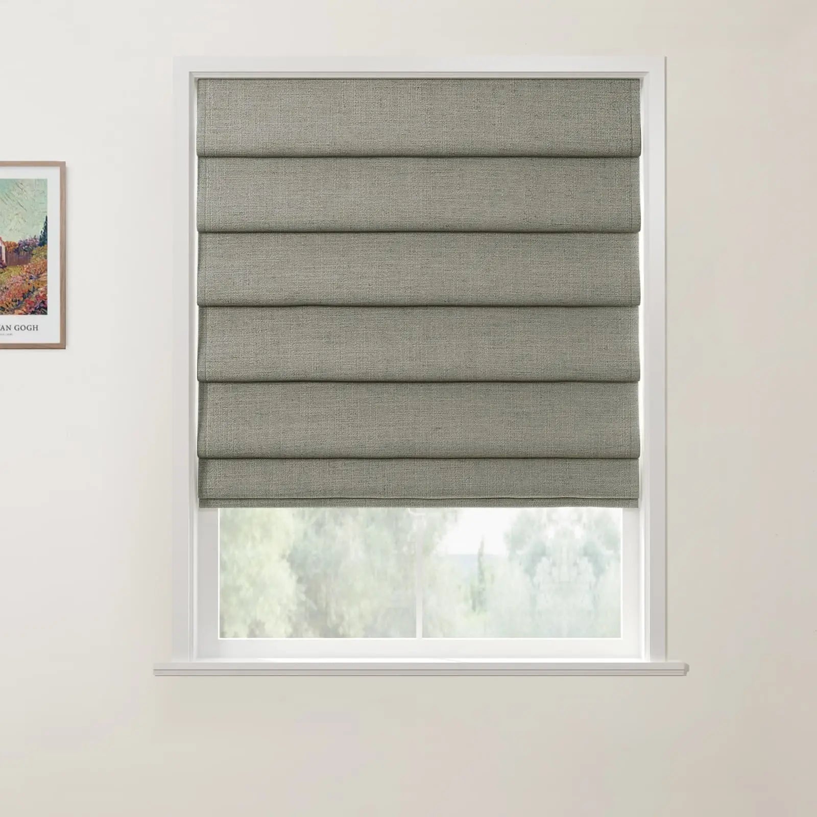 Photograph of a window in an interior room featuring a textured grey-green roman blind with stacked horizontal folds, a glimpse of blurred green trees outside, and a framed Van Gogh landscape print with a colorful house on the left wall