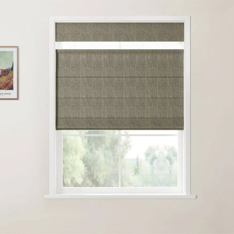 An interior view of a window fitted with a textured greige Roman blind partially raised above a soft green outdoor landscape complemented by a framed Van Gogh print on the left wall