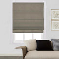 A photograph of a modern living room interior showcasing a window dressed with a medium grey Roman blind, a beige sofa featuring a unique curved armrest, and decorative pillows including a black and white houndstooth pattern, alongside two framed abstract art prints on the wall