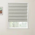 A modern window featuring a light grey textured Roman blind, set against an off-white wall with a visible Van Gogh painting detail on the left, looking out onto a soft green natural landscape