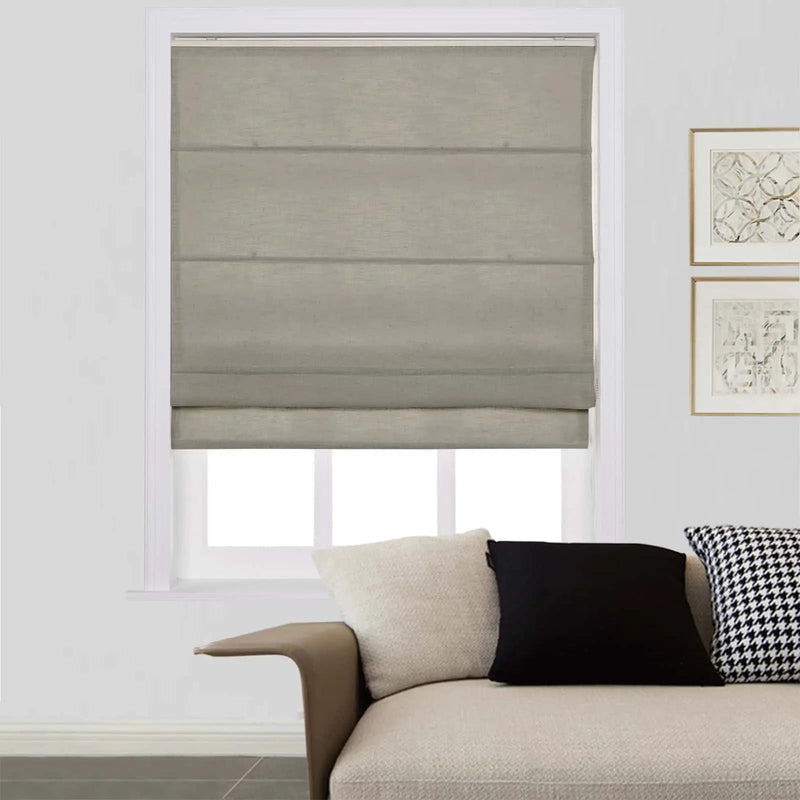 A modern living room interior featuring a grey Roman blind on a window, a neutral sectional sofa adorned with cream textured, solid black, and black and white houndstooth pillows, and two gold-framed abstract art prints on the wall