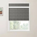 Photograph of an interior window with dark grey textured Roman blinds, a white frame, and a print of Van Gogh's The Red Vineyard on the wall showing blurred green trees outside