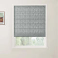 A grey textured Roman blind is partially lowered over a window in a light-colored room revealing a soft green foliage view outside and a framed Van Gogh print on the left wall