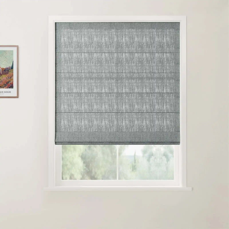 A grey textured Roman blind is partially lowered over a window in a light-colored room revealing a soft green foliage view outside and a framed Van Gogh print on the left wall