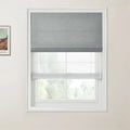 Photograph featuring a Van Gogh landscape print beside a modern interior window with a grey textured Roman shade, a sheer lower blind, and white frame looking out to blurred green trees
