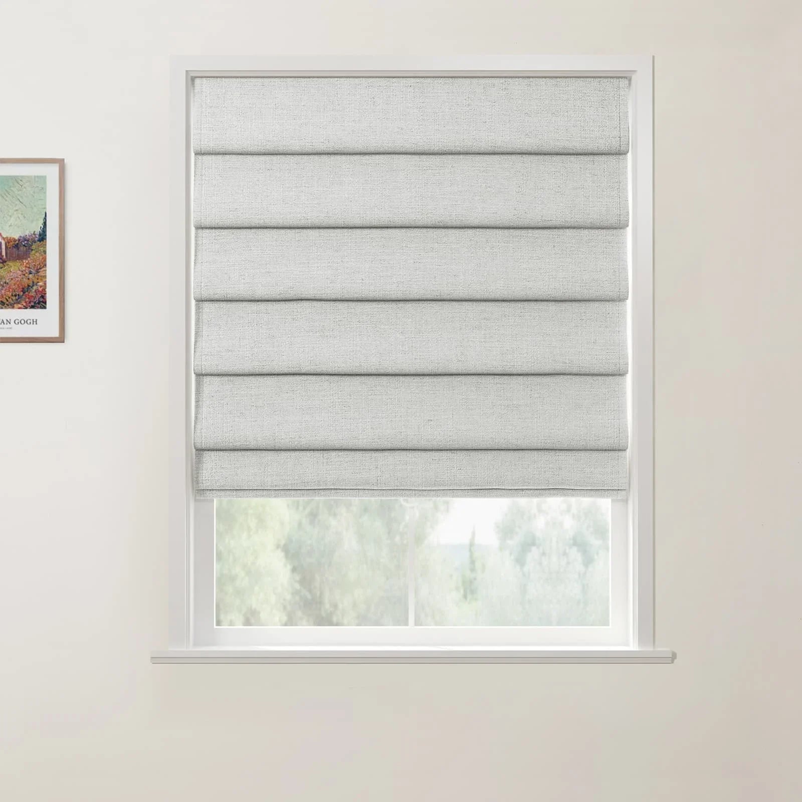 Framed print of a Van Gogh painting hanging next to a window featuring a light grey textured Roman blind in an interior room with white walls overlooking blurred green foliage