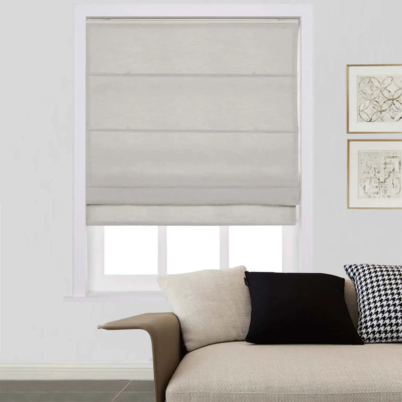 Interior scene showing a window fitted with a light beige Roman blind, an off-white textured sofa with cream, black, and houndstooth pattern cushions, and two gold-framed abstract artworks on the adjacent wall