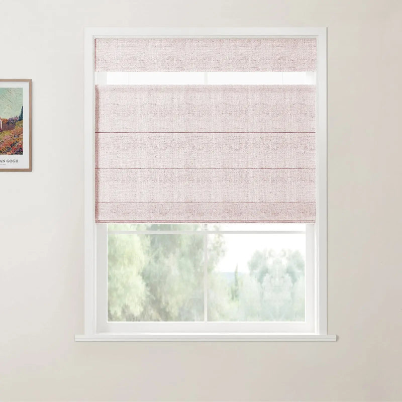 Photograph of a white-framed window showcasing a light pink textured Roman blind with a top-down bottom-up feature, revealing lush green trees outside and a framed Van Gogh art print on the left wall