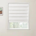 Photograph of a textured white Roman blind covering most of a white window frame, revealing blurry green trees outside, with a framed colorful Van Gogh landscape print on the adjacent light wall