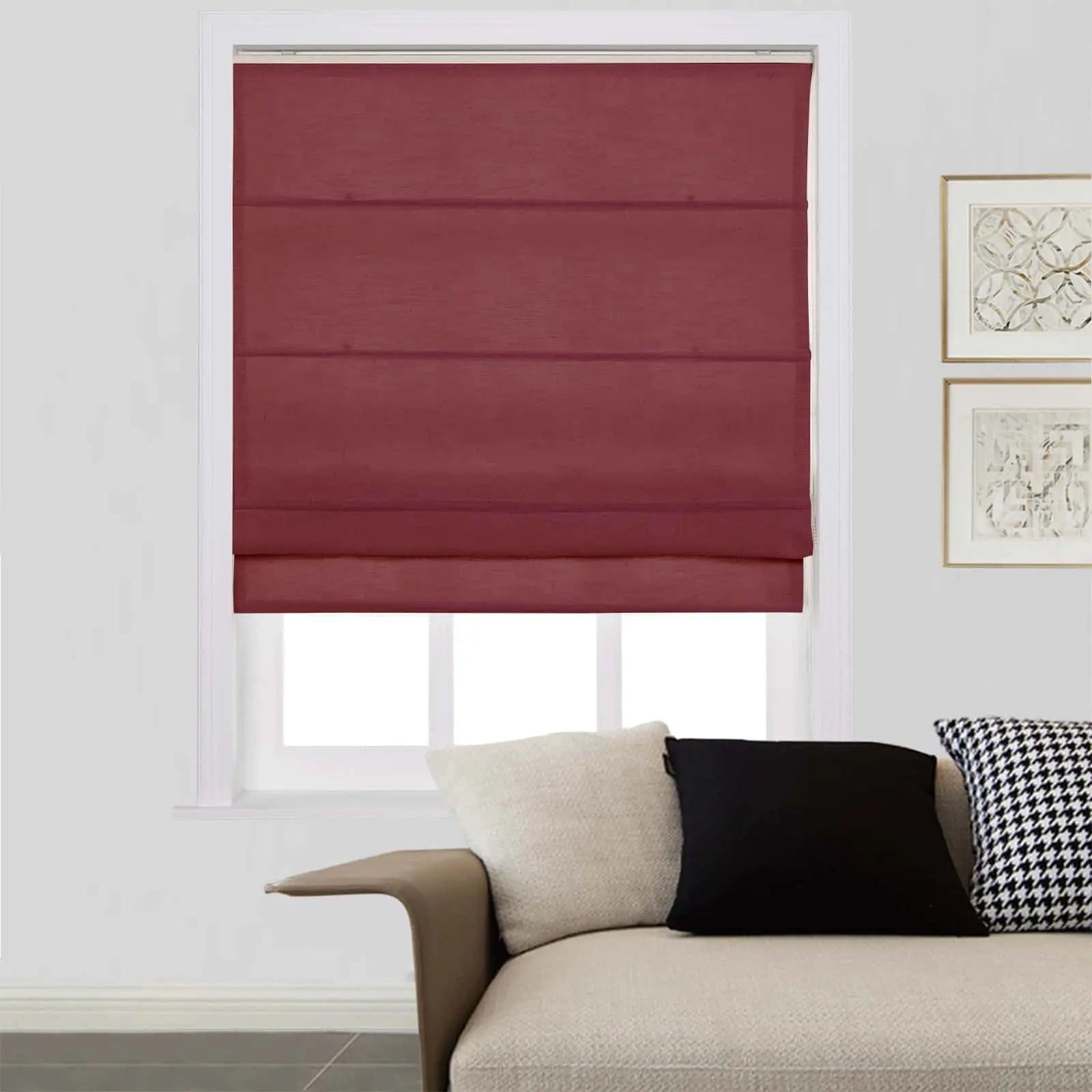 A maroon Roman blind covers most of a bright white window, situated above a beige modern sofa with an off-white, black, and distinctive black-and-white houndstooth pillow, with framed abstract art on the wall
