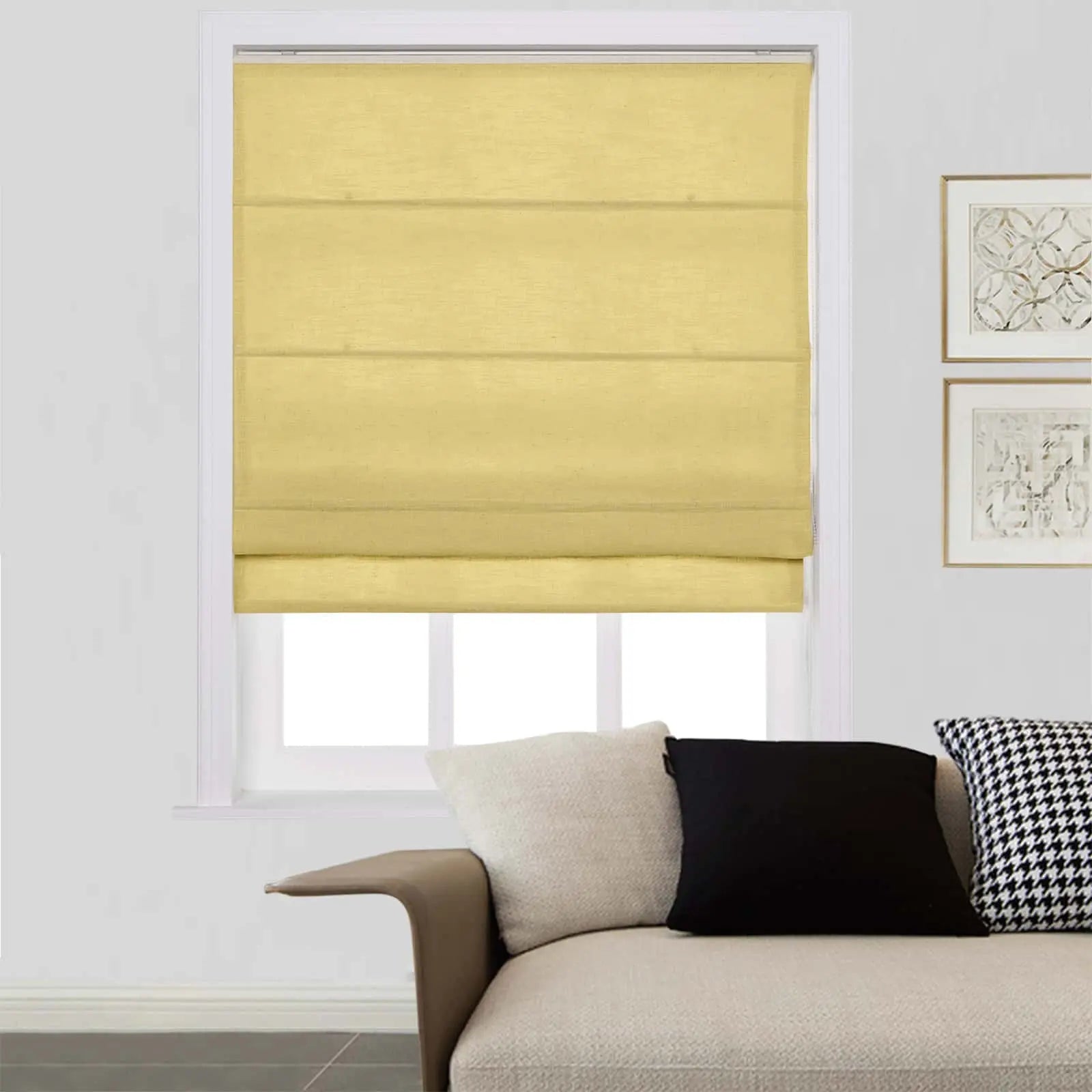 A modern living room interior featuring a window with a bright yellow Roman shade, part of a beige textured sofa accessorized with a black solid pillow and a black and white houndstooth pillow, and two framed abstract prints on the white wall