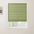 Photograph of a window in a white room featuring a textured light green Roman blind partially raised, revealing a blurred natural outdoor scene through the white frame