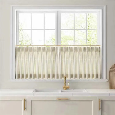 Ivory White Liz cafe curtain covering the lower half of a bright kitchen window above white cabinetry and a brass tap