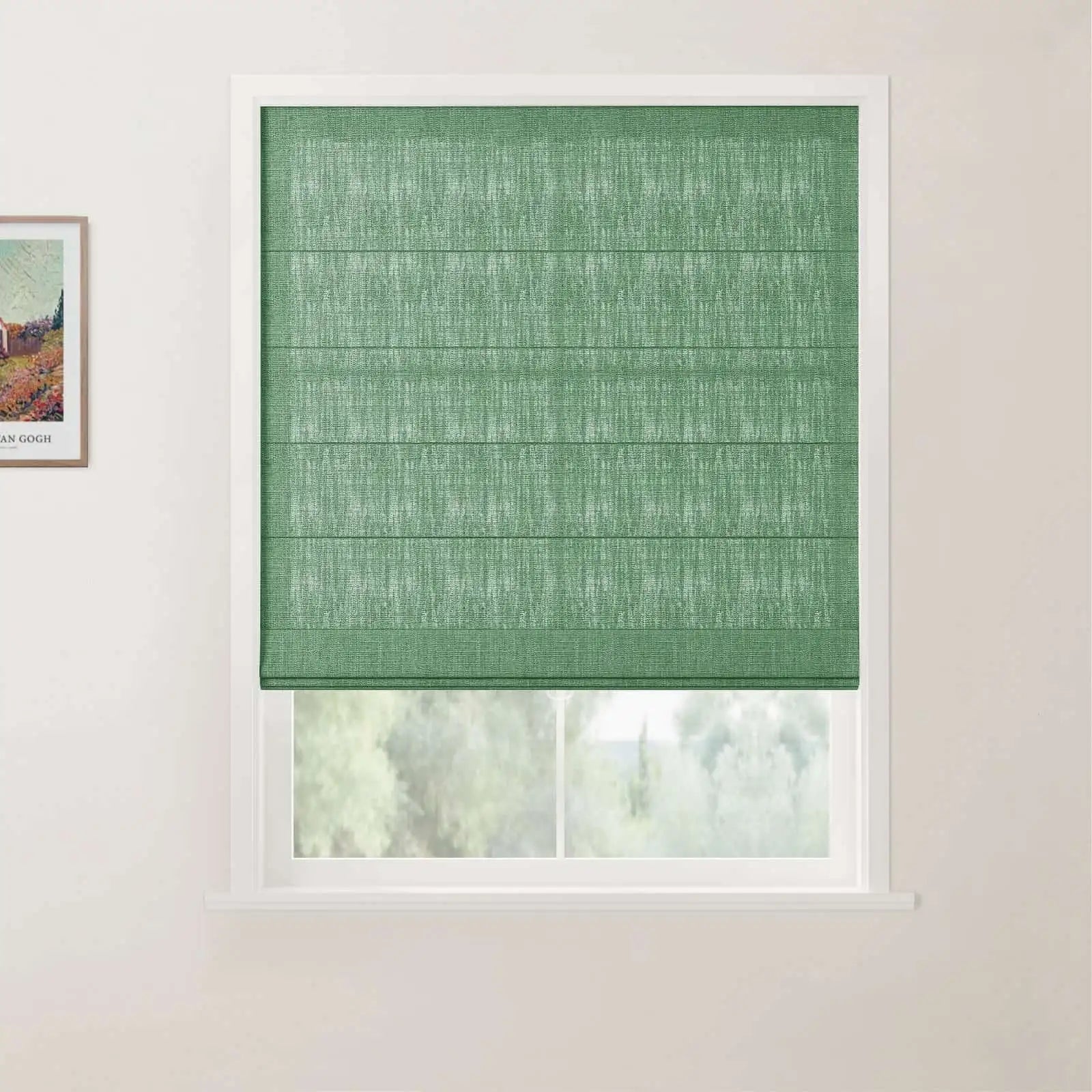 Photograph of a window with a textured sage green Roman blind featuring horizontal folds, set in a white frame against a light beige wall with a framed Van Gogh print to the left