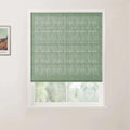 Photograph of a window in a room featuring a textured sage green Roman blind, white frame and sill, blurred green trees outside, and a framed Van Gogh print on the left wall