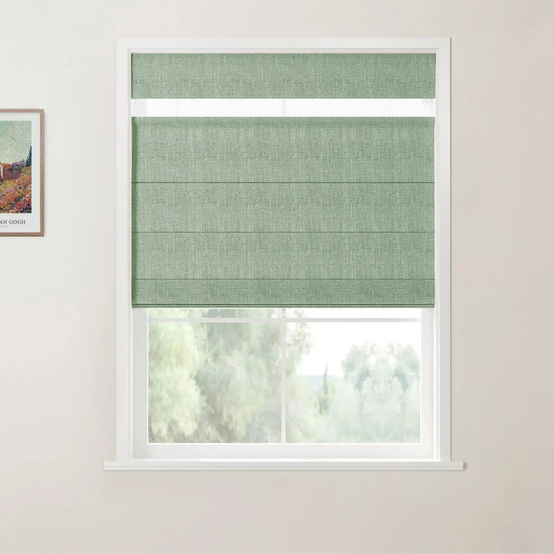Photograph featuring a textured sage green Roman blind on a white window frame, with a framed Van Gogh landscape print visible on the adjacent wall and blurry green trees outside