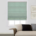 A mint green fabric roman shade fully covers a window in a contemporary living room, with a beige textured sofa and two gold-framed abstract prints