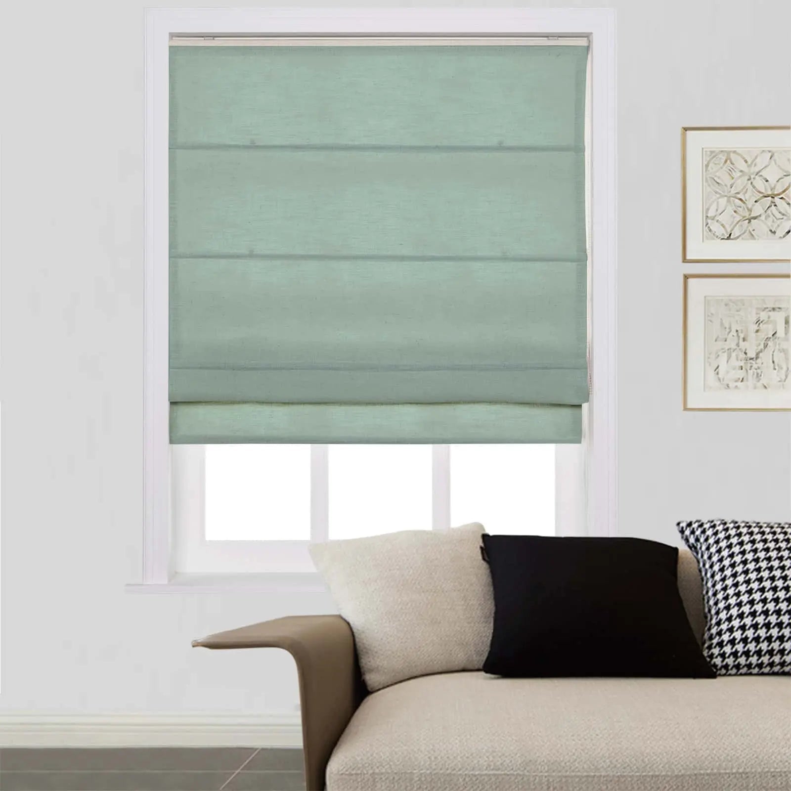 A mint green fabric roman shade fully covers a window in a contemporary living room, with a beige textured sofa and two gold-framed abstract prints