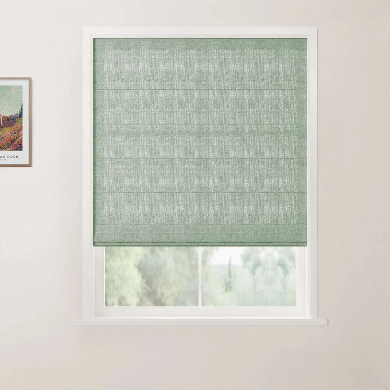 A sage green textured Roman blind with horizontal folds in a white window frame, partially revealing a blurry green landscape outside, with a framed Van Gogh print on the adjacent wall