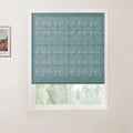 A modern interior window featuring a vibrant teal blue textured Roman blind partially open to reveal green foliage outside, with a framed Van Gogh landscape print visible on the adjacent white wall
