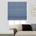 A modern living room featuring a blue fabric Roman shade on a window above a beige textured sofa with black, white, and houndstooth pillows and gold-framed wall art
