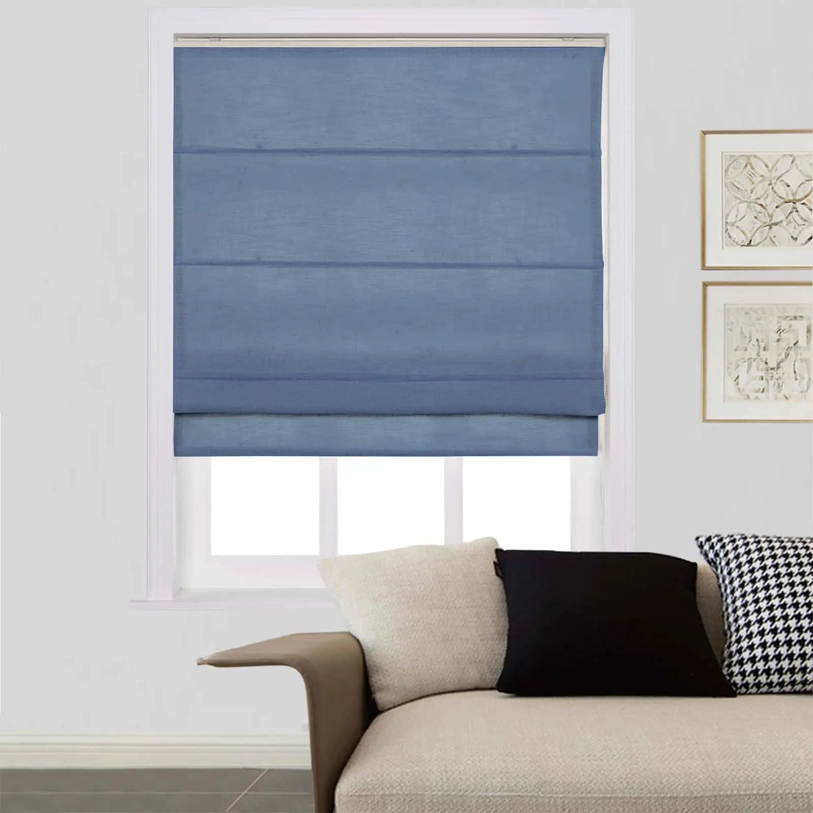 A modern living room featuring a blue fabric Roman shade on a window above a beige textured sofa with black, white, and houndstooth pillows and gold-framed wall art