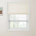 Photograph of an interior window with a textured off-white top-down Roman blind over a sheer light grey bottom-up Roman blind, a partially visible framed Van Gogh print on the adjacent wall, and blurred green foliage outside