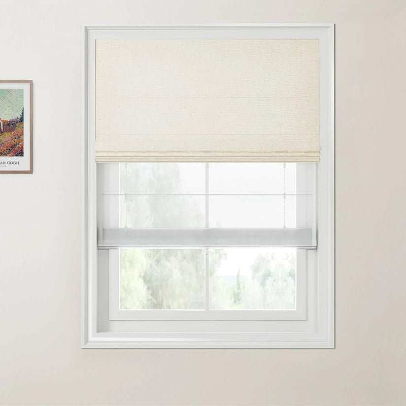 Photograph of an interior window with a textured off-white top-down Roman blind over a sheer light grey bottom-up Roman blind, a partially visible framed Van Gogh print on the adjacent wall, and blurred green foliage outside
