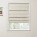 A photograph showing a window in an interior room with a textured beige Roman blind half-closed revealing a view of green trees, and a framed Van Gogh landscape print on the adjacent white wall