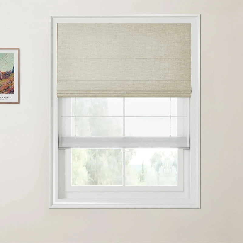 Photograph of a modern interior window featuring a beige textured Roman shade over a sheer white blind with a framed Van Gogh landscape artwork on the left wall and blurry green trees outside