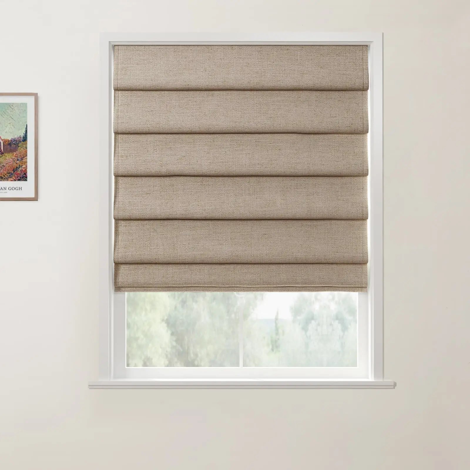 Photograph of a window featuring natural beige linen Roman shades in a white interior with a subtle outdoor view of green foliage and a framed Van Gogh print on the adjacent wall