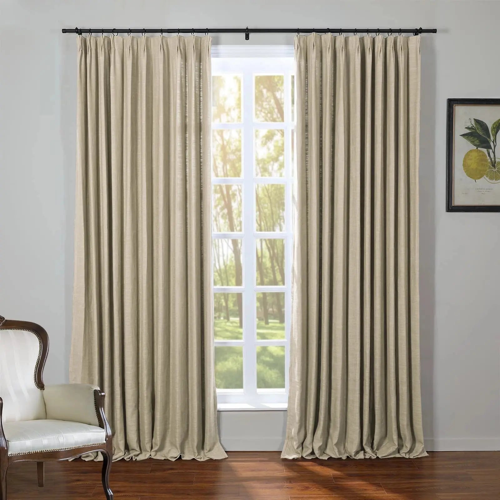 A room with floor-length beige linen curtains on a black rod framing a white-paned window revealing a sunny green forest complemented by a cream upholstered classic wooden chair and a framed lemon botanical print on a gray wall