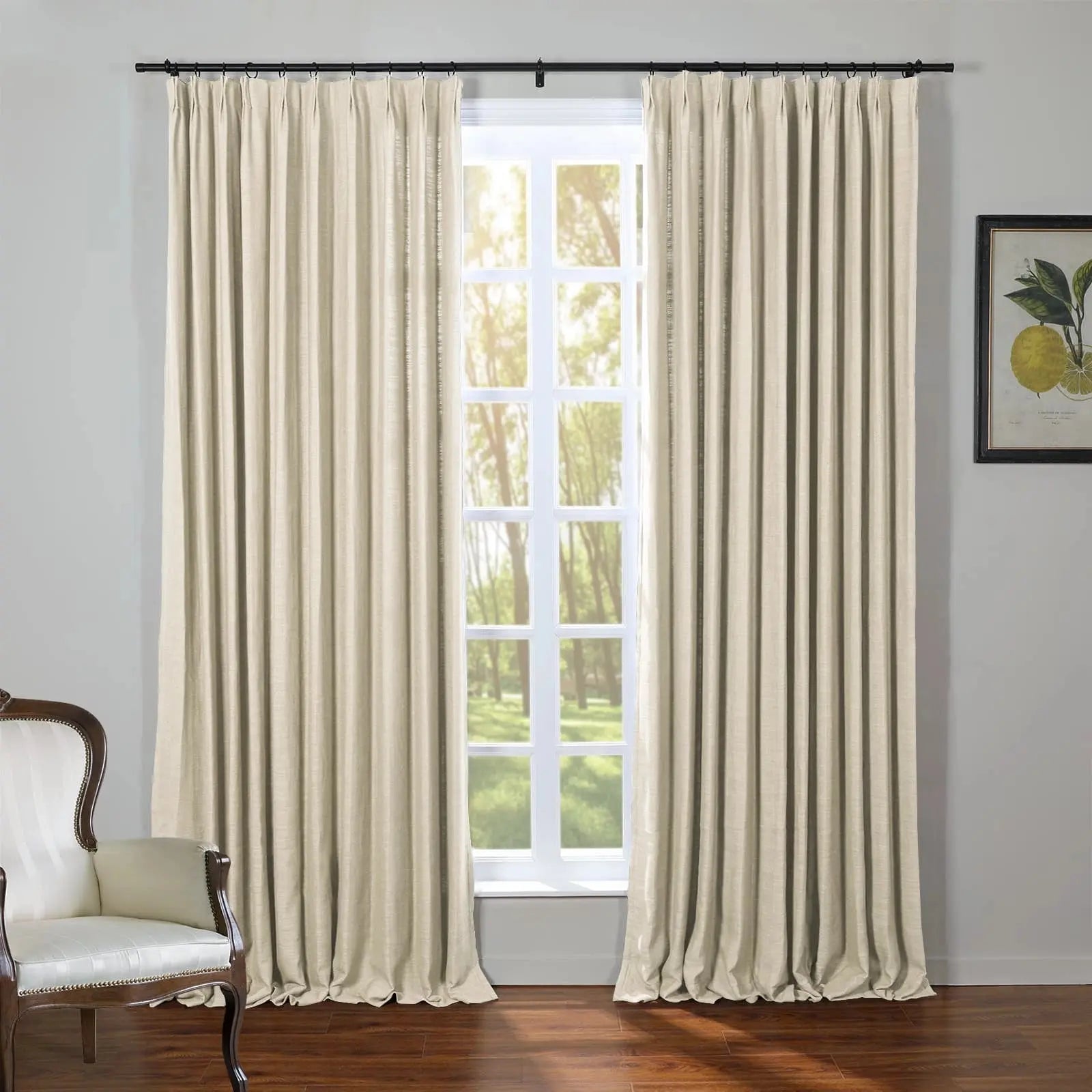 Photograph of a room featuring a large white paned window flanked by full-length beige pinch-pleat drapes, with a vintage wooden chair upholstered in white stripes and a framed botanical print of yellow lemons, overlooking a sunlit green treed landscape