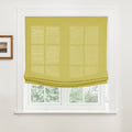 Photograph of a white-trimmed window featuring a vibrant chartreuse Roman blind partially raised with visible layered folds overlooking green trees with a small framed landscape artwork on the adjacent wall