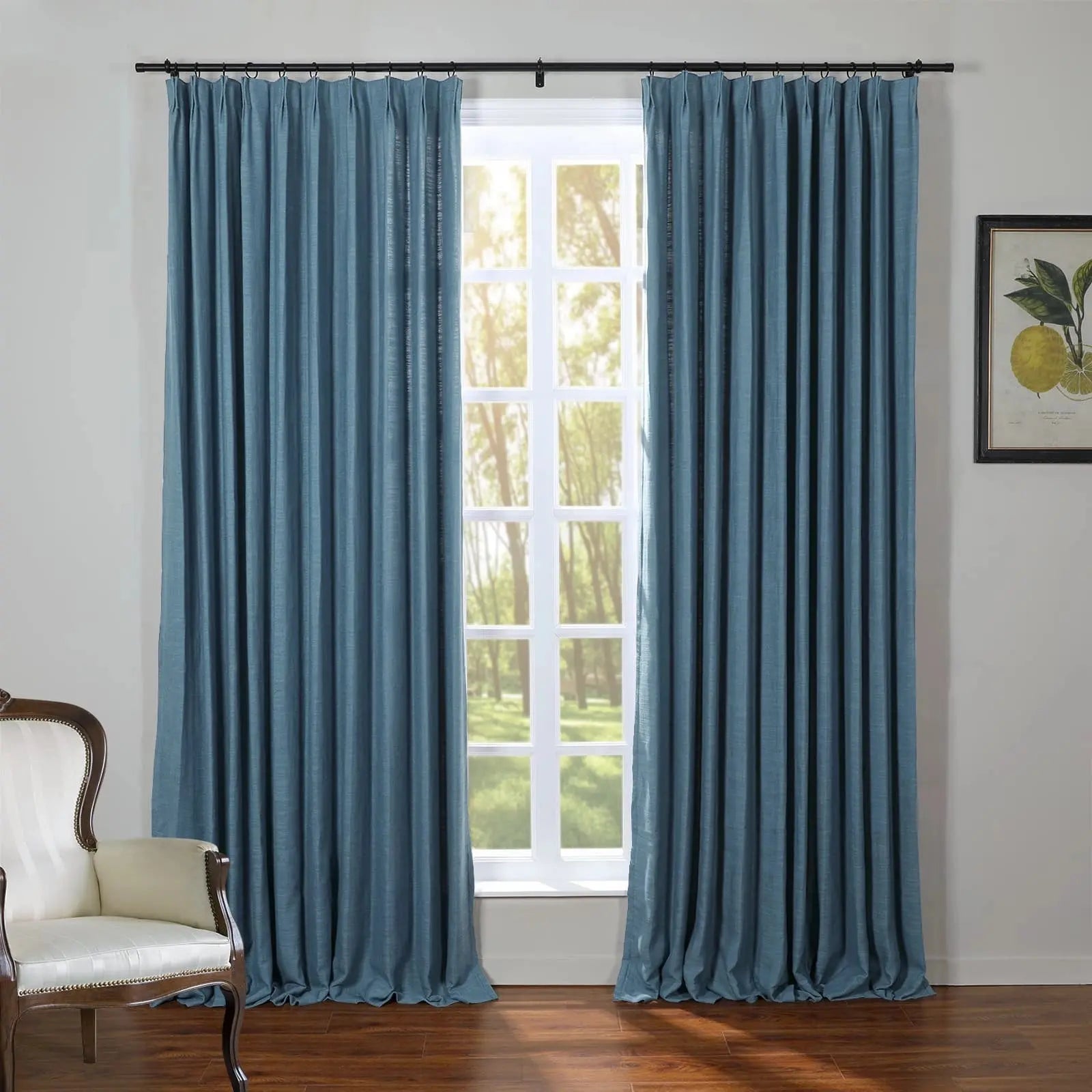 Teal blue linen-look curtains frame a multi-pane window in an interior room, alongside a cream upholstered armchair and a framed lemon botanical print